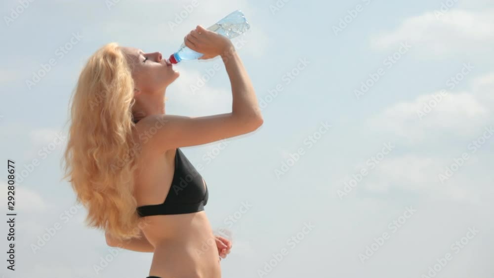 Blonde in a bikini drinks water from a bottle Blonde in a bikini drinks water from a bottle