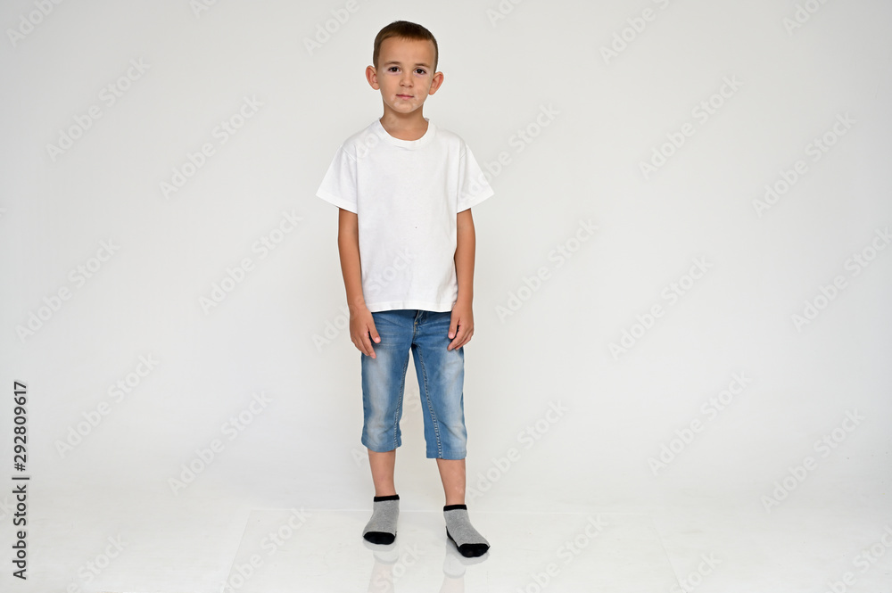 Full-length portrait on a white background of a cute boy child with Vitiligo disease - a violation of the color of the skin at the initial stage. White T-shirt, blue jeans. Full-length portrait on a white background of a cute boy child with Vitiligo disease - a violation of the color of the skin at the initial stage. White T-shirt, blue jeans.