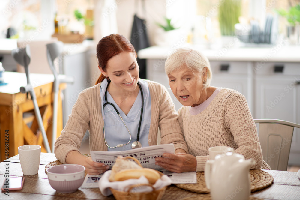 Caregiver reading morning news for retired woman Caregiver reading morning news for retired woman