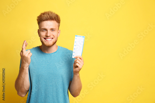 Konstfotografi Portrait of hopeful young man with crossed fingers holding lottery ticket on yel