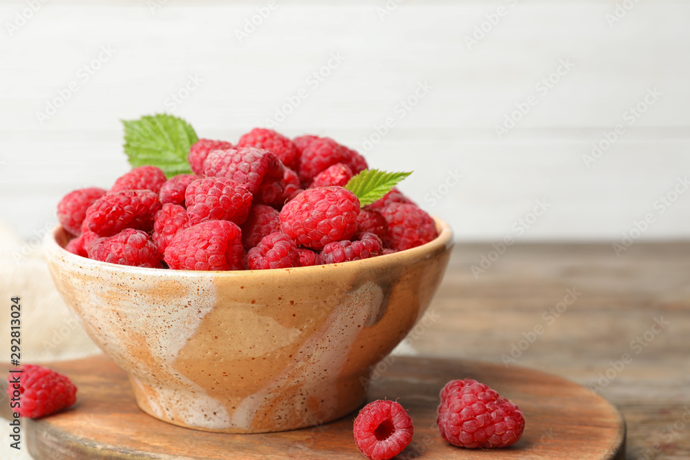 Bowl with delicious ripe raspberries on cutting board against light background, space for text Bowl with delicious ripe raspberries on cutting board against light background, space for text