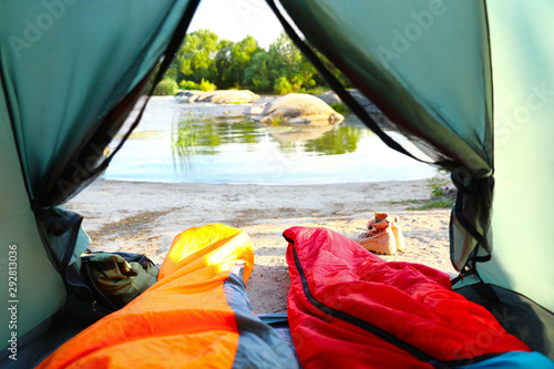 Camping tent with sleeping bags near lake, view from inside