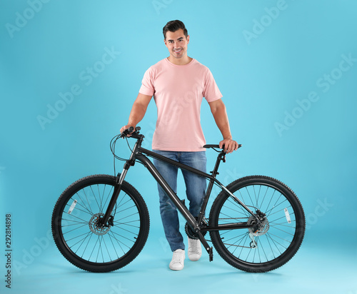 Handsome young man with modern bicycle on light blue background