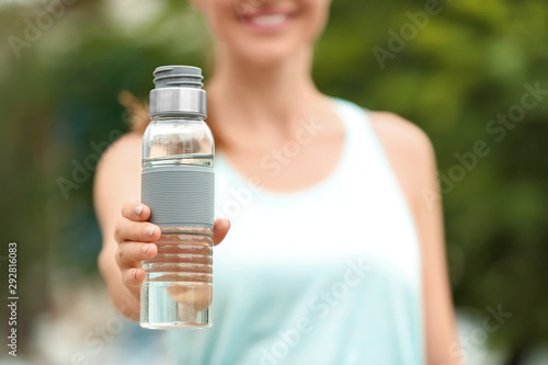 Young woman with bottle of water outdoors, closeup. Refreshing drink