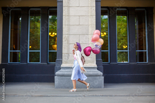 Girl with purple hair walking outdoor with bunch of helium baloons