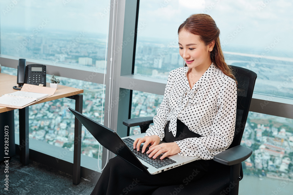 Smiling pretty female big company manager working on laptop in modern office