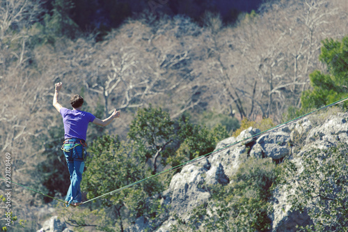 A man is walking along a stretched sling. Highline in the mountains. Man catches balance. Performance of a tightrope walker in nature. Highliner on the background of the mountains.