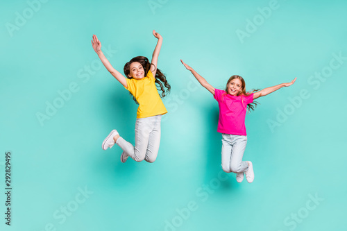 Full length body size photo of two enjoying girls being free wearing yellow and pink t-shirts while isolated with teal background