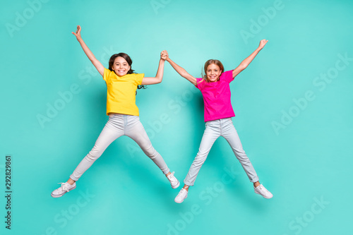 Full length body size photo of two nice cute beautiful people girls jumping like stars while isolated with teal background © deagreez