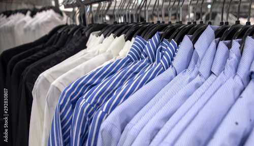 White and blue shirt on hang for sale in shop. Male wear on plastic hanger. Official wear for men in department store