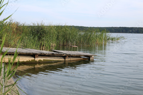 Forest lake in the evening. The wooden mooring for boats  is made of an old planks  on which there is a chair for fishing.