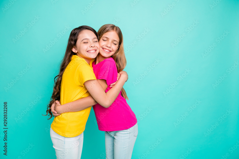 Photo of two hugging girls creating copyspace loving each other as best friends while isolated with teal background Photo of two hugging girls creating copyspace loving each other as best friends while isolated with teal background