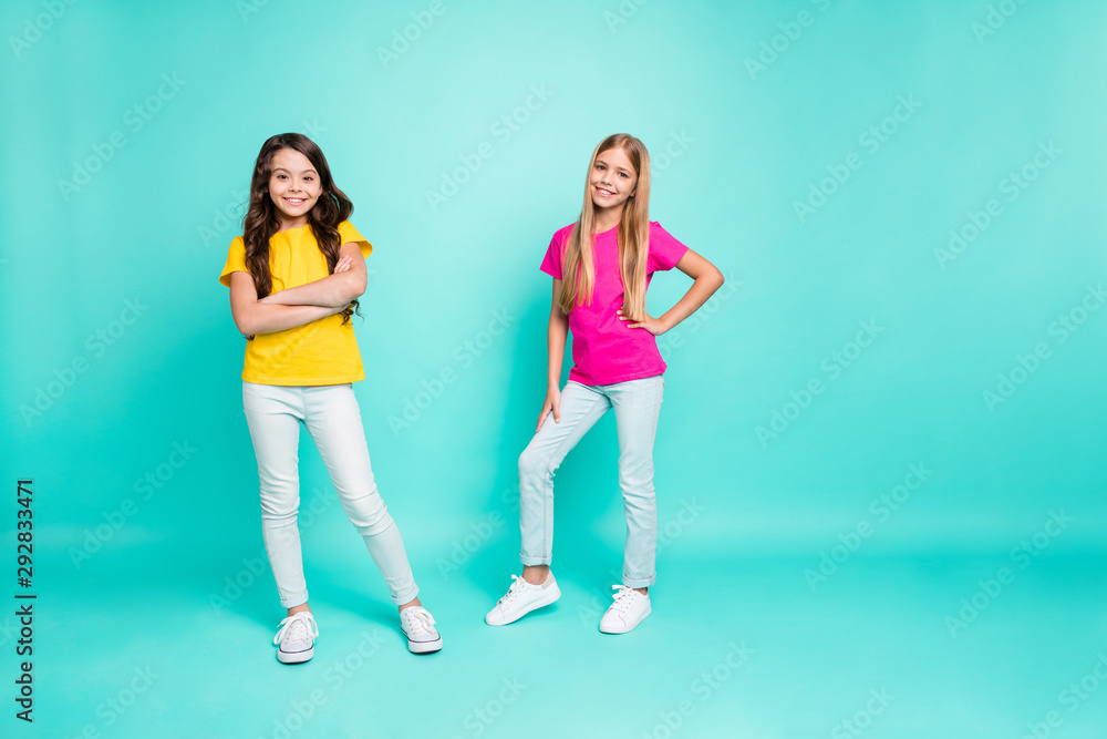 Fototapeta premium Full length body size photo of two young models posing in front of camera wearing pink and yellow t-shirts while isolated with turquoise background