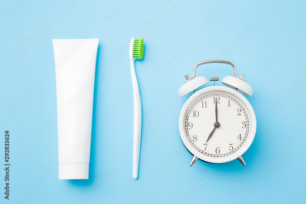 Alarm clock, toothbrush with green bristles and white tube of toothpaste on pastel blue background. Healthy teeth. Morning routine concept.  - obrazy, fototapety, plakaty 