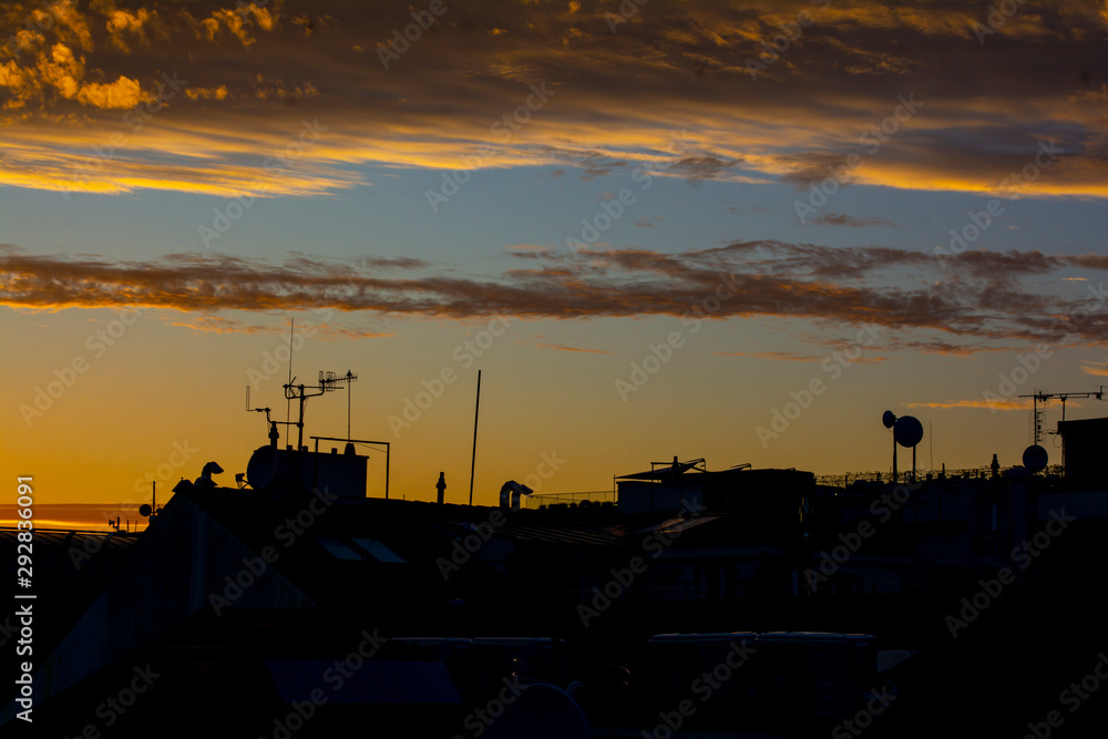 Black silhouette of city roofs with pipes and antennas against the sky at sunset