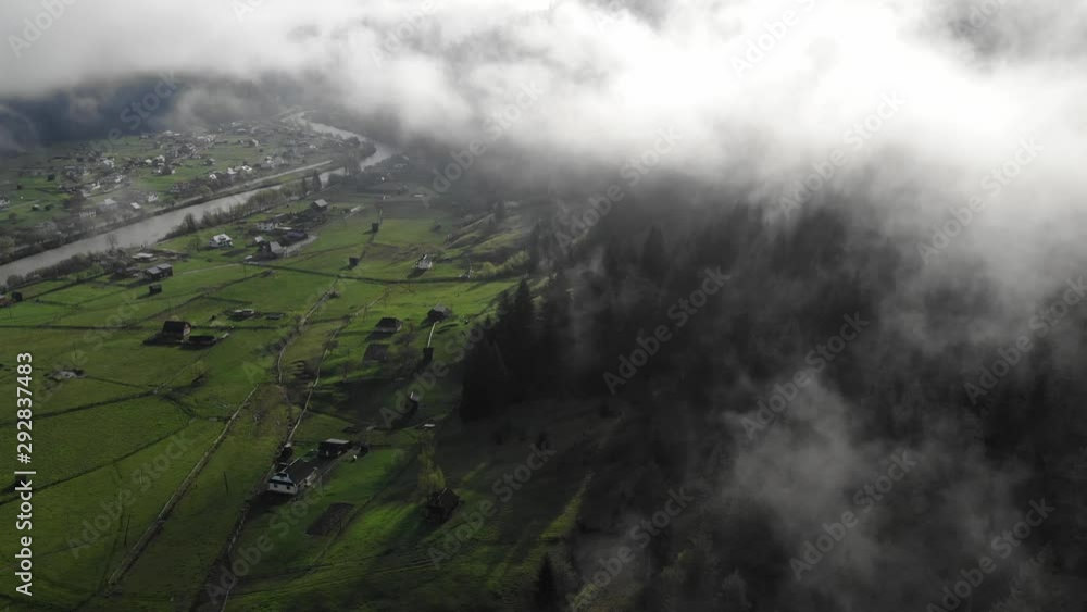 Aerial drone shot above fog in mountains and a small mountain town. Sunrise, fog cloudy sky over houses and river. Aerial drone shot above fog in mountains and a small mountain town. Sunrise, fog cloudy sky over houses and river.