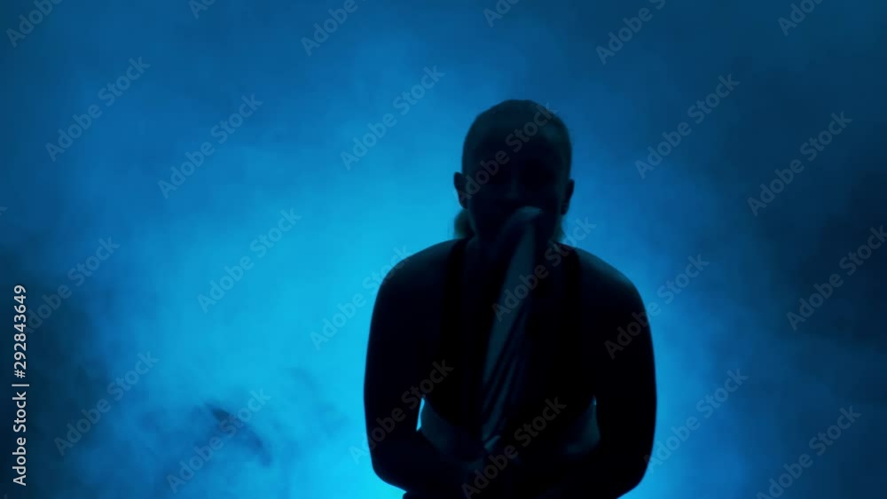 Silhouette of tennis player with a racket in hands on a dark background of blue smoke. Woman playing tennis. Silhouette of tennis player with a racket in hands on a dark background of blue smoke. Woman playing tennis.