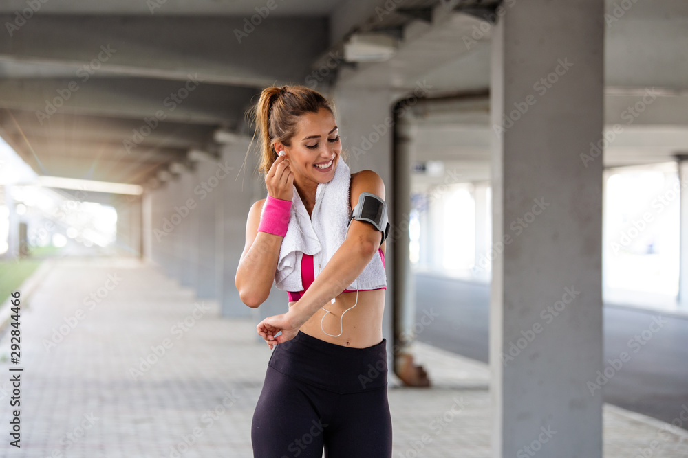 Fototapeta premium young beautiful woman jogging, fitness outfit, listening to music on headphones, smartphone, sea sunrise, skinny perfect slim body, healthy living lifestyle, summer, smiling, happy