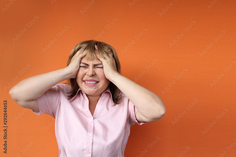 middle aged european woman holding her head, orange background, concept headache, stress, close-up, copy space middle aged european woman holding her head, orange background, concept headache, stress, close-up, copy space