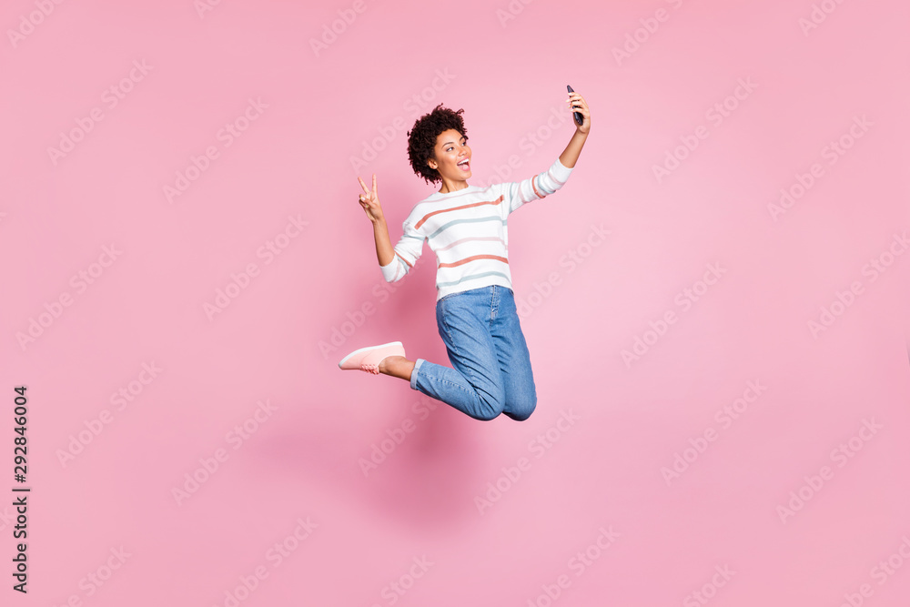 Full length body size photo of charming cheerful cute nice blogger jumping showing v-sign taking selfie wearing jeans denim white striped sweater expressing emotions on her face isolated pastel color
