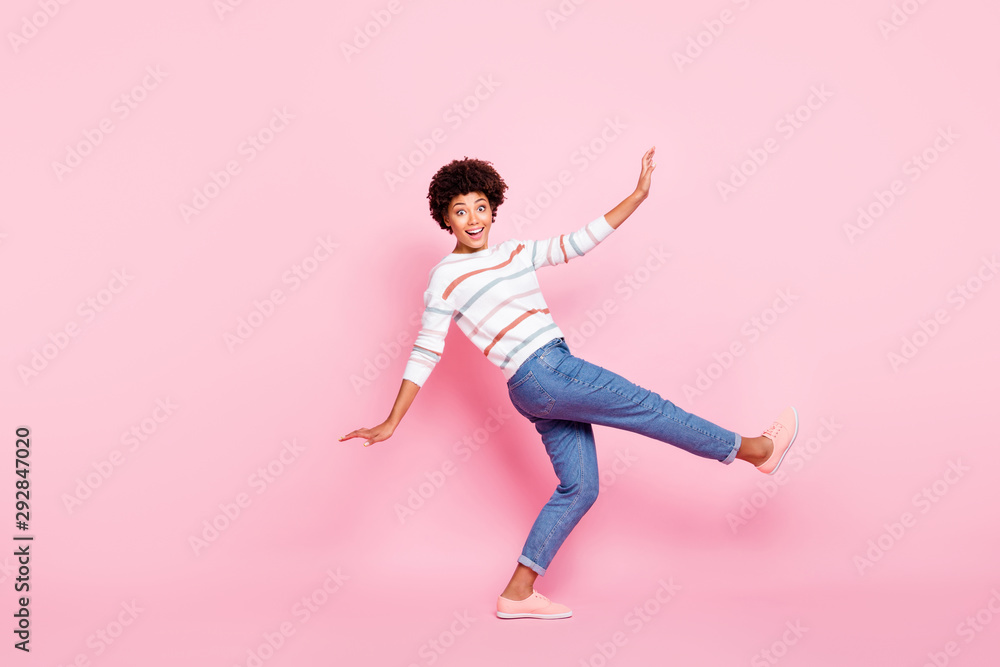 Full body profile photo of pretty dark skin lady at dancing class learning new modern moves wear striped pullover and jeans isolated pastel pink color background