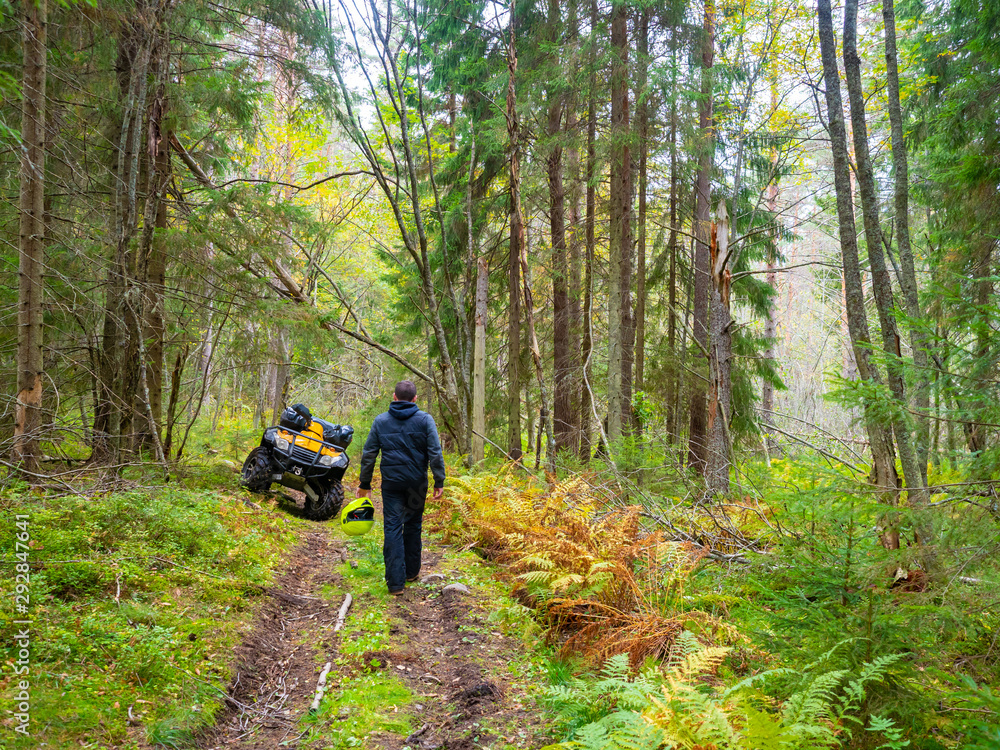 A man with a yellow helmet goes to ATV. Quad Biking in the woods. Outdoor activities. Rent ATVs. Quad bike control. Yellow ATV on a forest road.