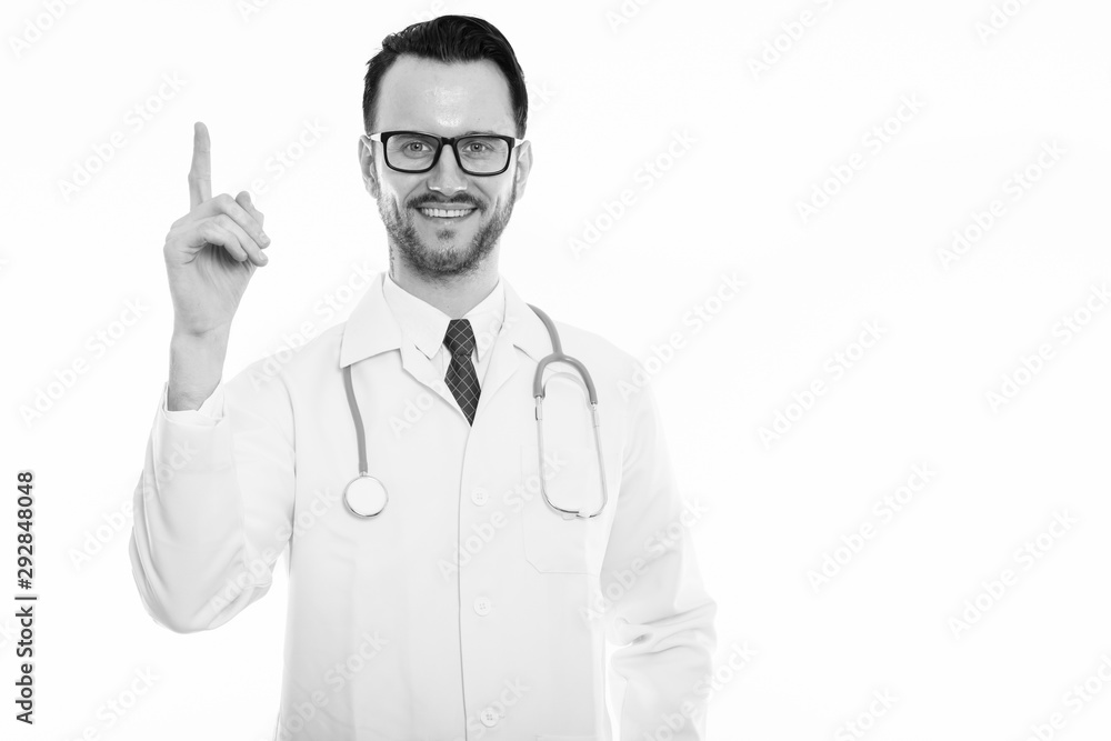 Studio shot of young happy man doctor smiling while pointing finger up