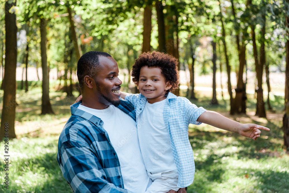 handsome father holding in arms happy kid pointing with finger in park handsome father holding in arms happy kid pointing with finger in park