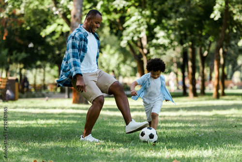 Happy African American man playing football with curly son