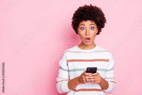 Photo of pretty dark skin lady holding telephone open mouth after reading shocking feedback wear striped pullover isolated pastel pink color background
