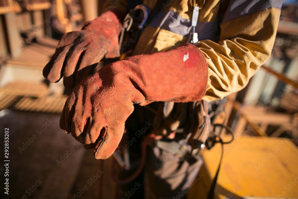 Male rope access worker welder hand preparing, wearing safety industry heavy duty reinforced quality leather gauntlet welding glove protection prior to commencing hot work on construction site, Perth 