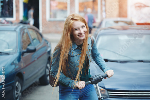 pretty young smiling redhead female student riding blue electric kick scooter 