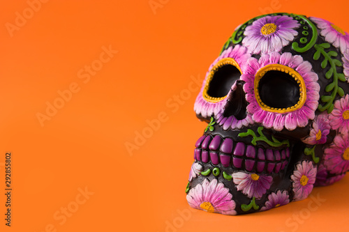Typical Mexican skull with flowers painted on orange background. Dia de los muertos. Copy space