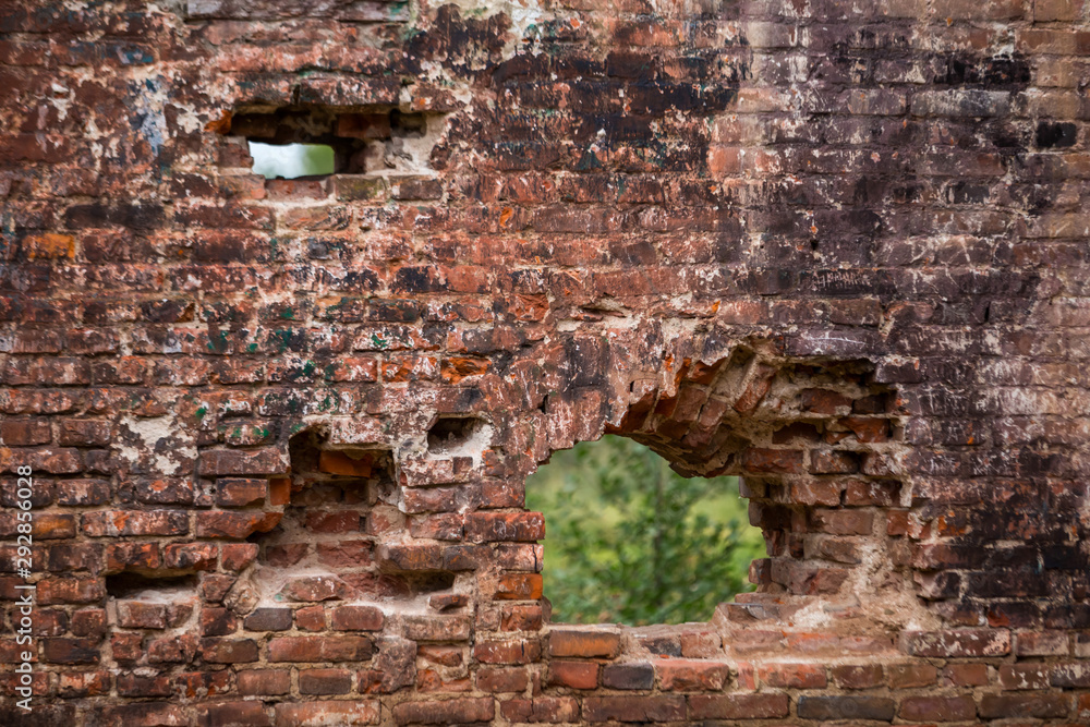 Old brick wall with through holes from the bombing, through which you can see the lush summer greenery.