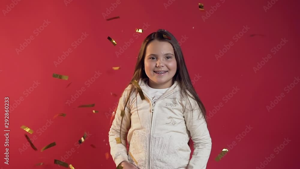 Close up of exuberant jolly teen girl dressed in stylish clothes throwing confetti on the red background Close up of exuberant jolly teen girl dressed in stylish clothes throwing confetti on the red background