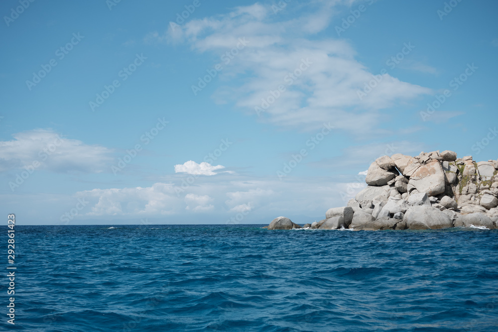 Seascape view from boat with anthropomorphic rock formation in a sunny day and clear blue sky and clouds in Sardinia.