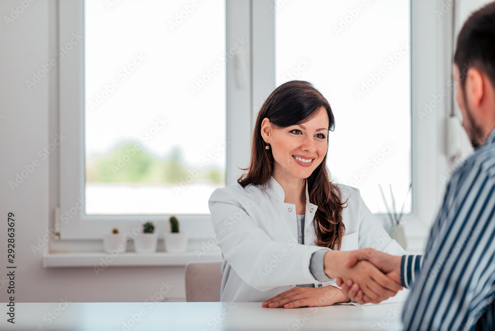 Portrait of a smiling female doctor handshake with a patient while sitting in the medical office. Portrait of a smiling female doctor handshake with a patient while sitting in the medical office.