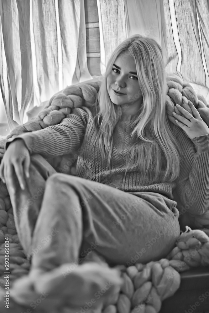 Fototapeta premium winter home interior, model girl basking in a knitted blanket at the window, a cold day at home