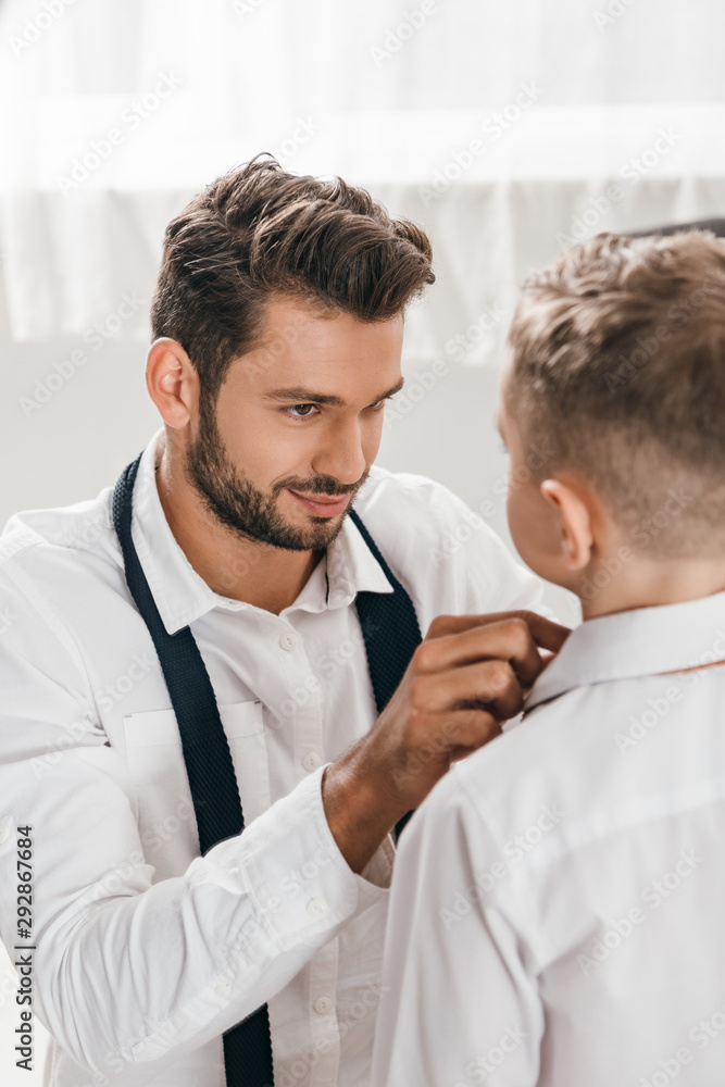 Obraz premium smiling father helping son to get dressed at home