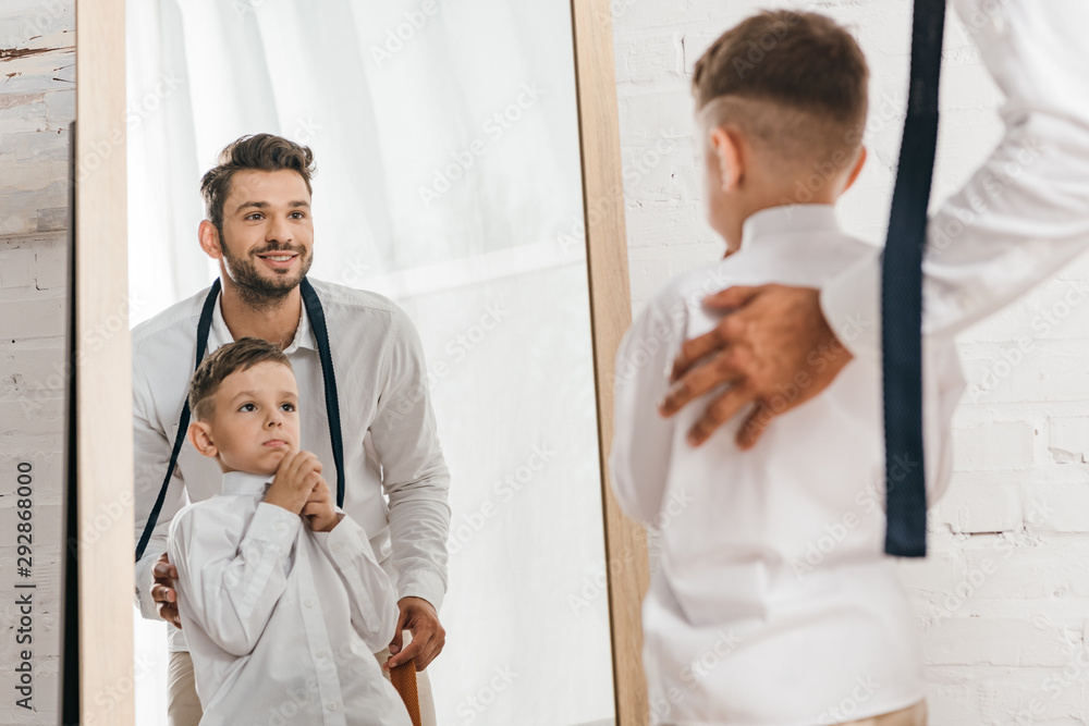 Obraz premium smiling dad and son in white shirts looking at mirror
