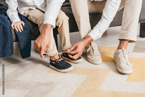 partial view of father teaching son to tying shoelaces at home