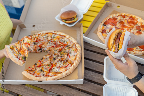 Eating out on summer terrace with italian cheesy pizza and juicy hamburger