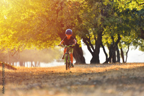 Happy kid boy of 7 years having fun in autumn park with a bicycle on beautiful fall day. Active child wearing bike helmet © Daniel CHETRONI