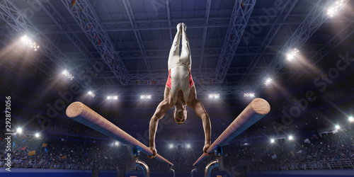 Male athlete doing a complicated exciting trick on parallel bars in a professional gym. Man perform stunt in bright sports clothes