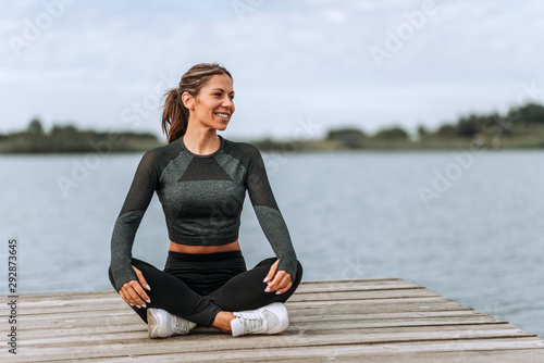 Smiling athletic woman sitting on a wooden river pier, relaxing.