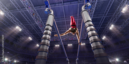 Tableau sur toile Male athlete doing a complicated exciting trick on parallel bars in a professional gym