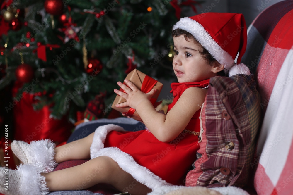 Merry Christmas and Happy New Year! Portrait of an emotional child in a New Year costume. Toddler girl in the decorated room with Christmas tree and new year decorations. Merry Christmas and Happy New Year! Portrait of an emotional child in a New Year costume. Toddler girl in the decorated room with Christmas tree and new year decorations.
