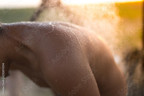 A silhouette of a man took a shower on the beach during sunset  focused on the man and vaguely on a drop of water