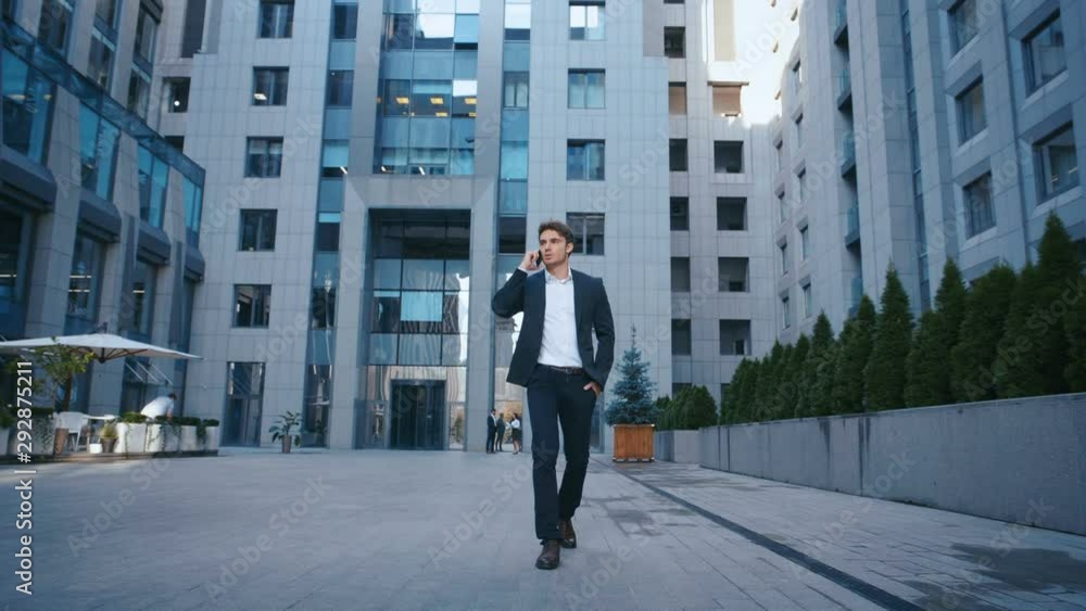 Successful Businessman Walking on Streets of Business District and talking on Mobile Phone. Confident attractive caucasian man in suit walking outside near big office building and using smartphone. Successful Businessman Walking on Streets of Business District and talking on Mobile Phone. Confident attractive caucasian man in suit walking outside near big office building and using smartphone.
