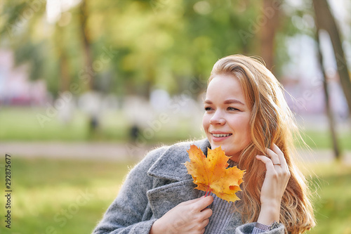 close-up portrait of a young woman with maple leaf in a park in golden autumn